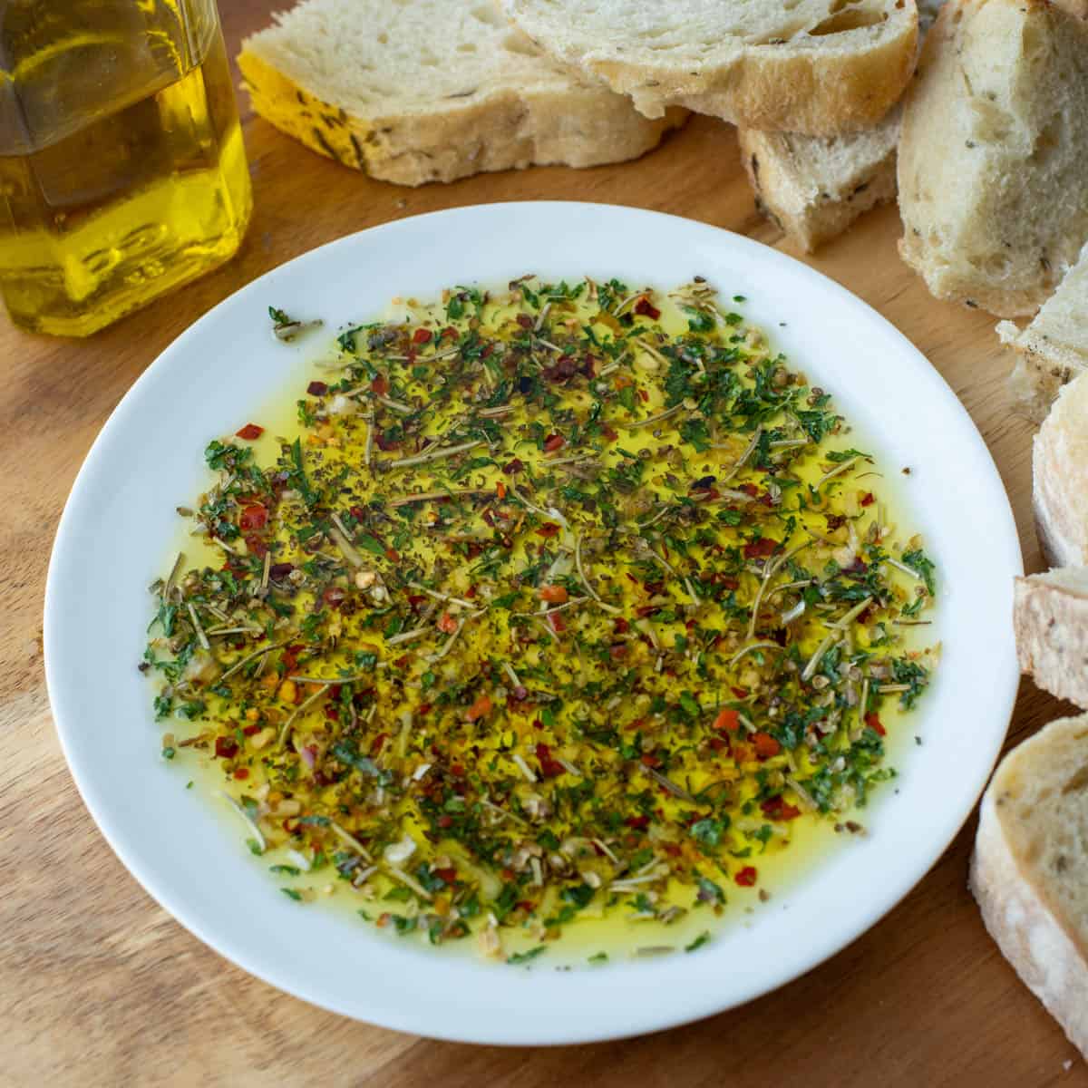 Bread dipper seasoning in oil on plate with bread and olive oil in the background