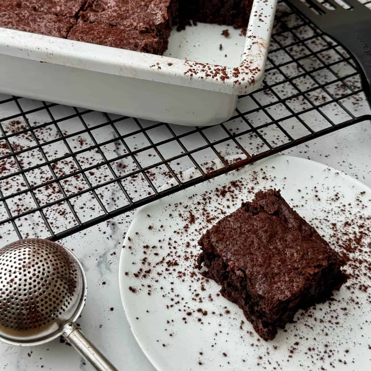 Close up of one brownie on plate with brownie pan in backgroundd