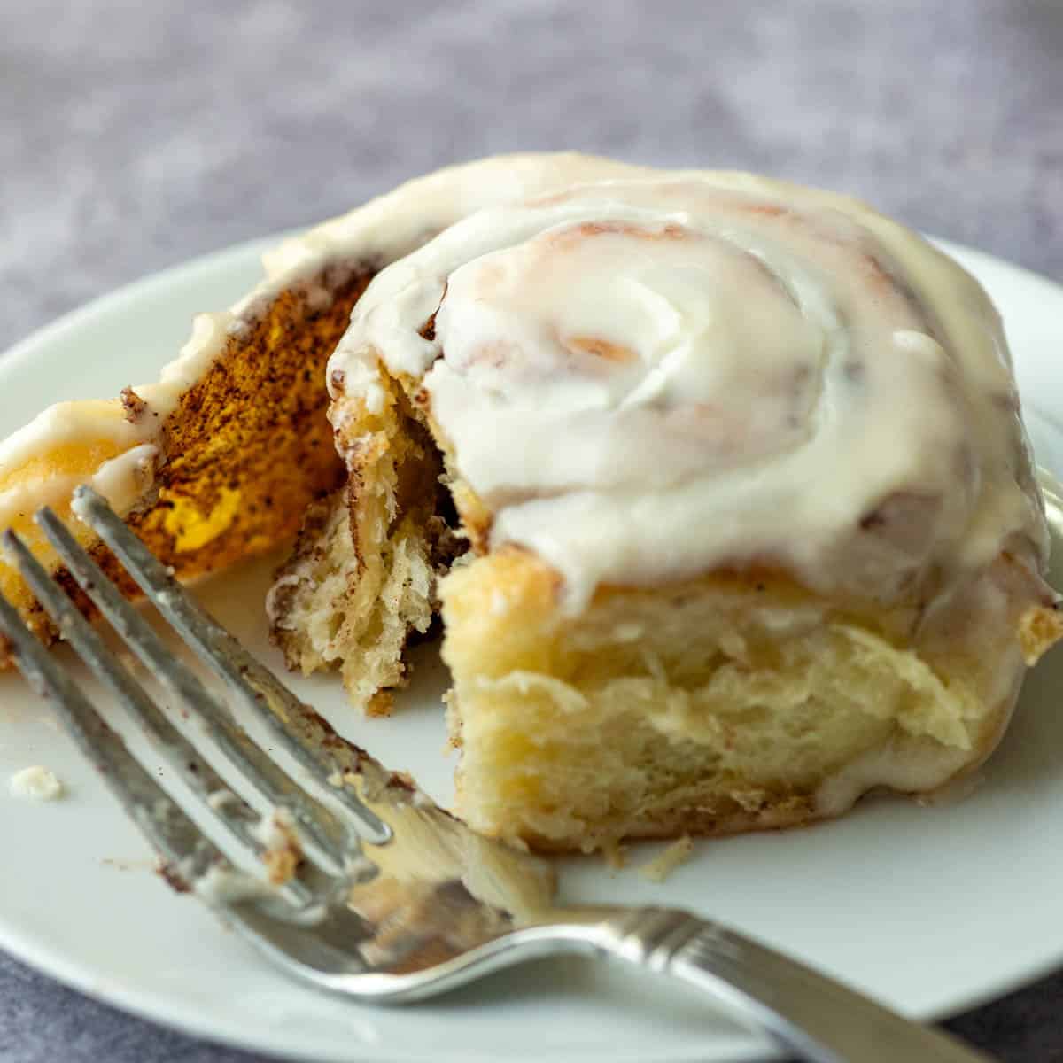 One partially eaten cinnamon roll on plate with fork 