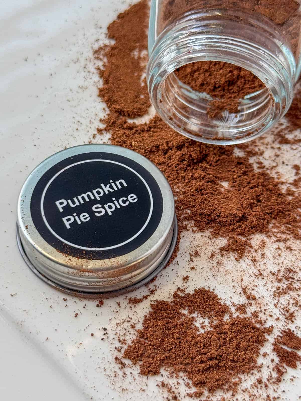 Jar of opened Pumpkin Pie Spice tipped on its side with loose spices in front