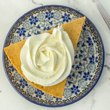 Individual slice of pumpkin cheesecake with whipped topping in shape of a rosette