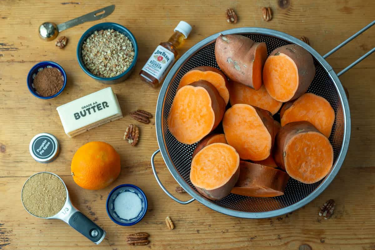 Photo of ingredients needs to make bourbon sweet potatoes: sweet potatoes, bourbon, butter, brown sugar, orange, pumpkin pie spice, salt and pecan pieces