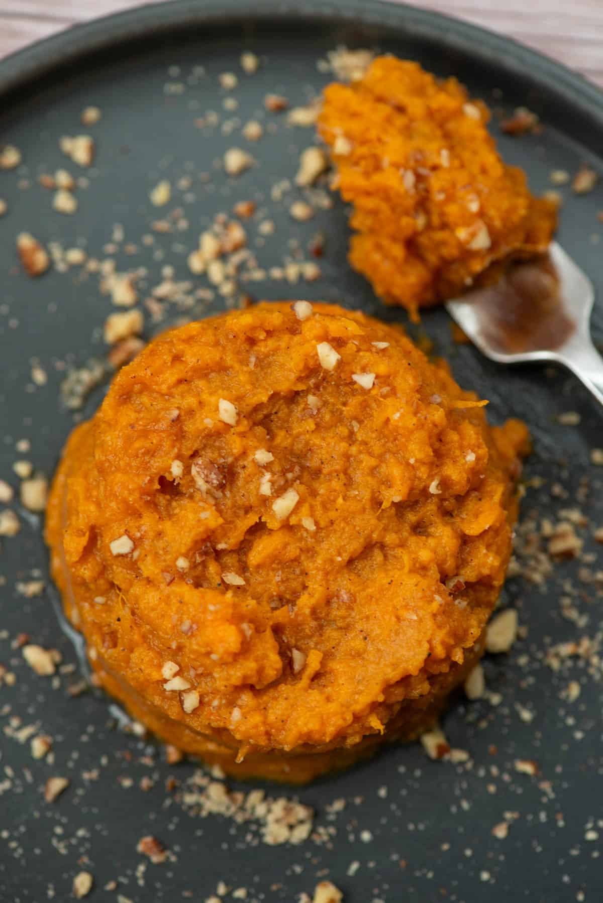 Close up photo of bourbon sweet potatoes on a plate with a fork and garnished with pecan pieces