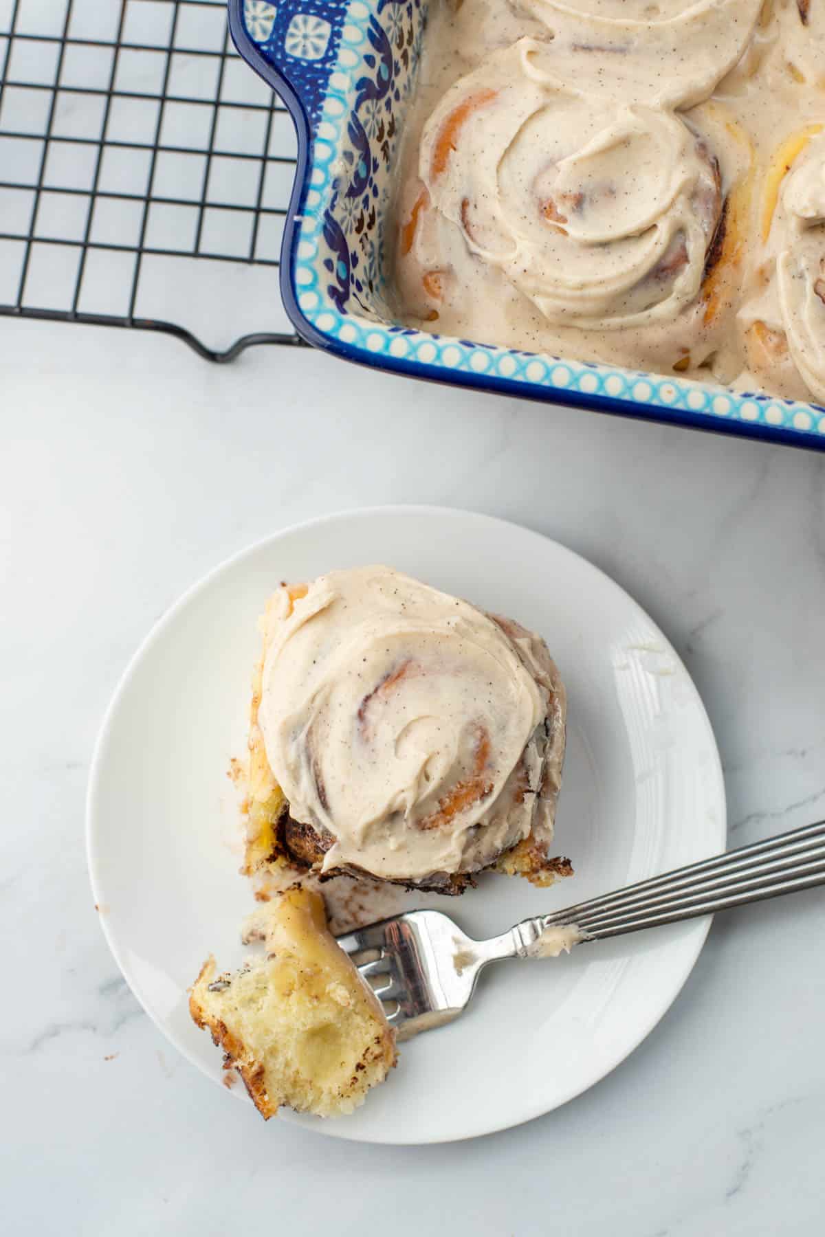 Chocolate sweet roll with espresso frosting on plate with pan of chocolate sweet rolls in background