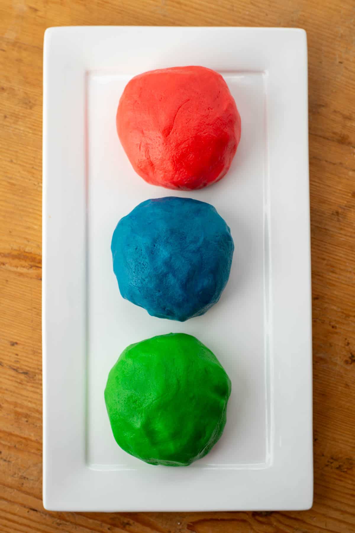 Pictures of raw colored cookie dough in balls. Red, blue and green balls