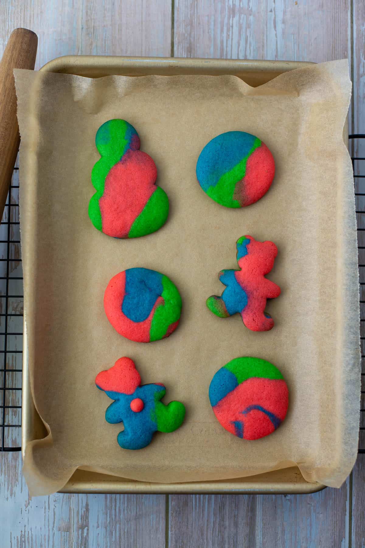 Photo of six colored cookie dough sugar cut out cookies on parchment paper on a cookie sheet