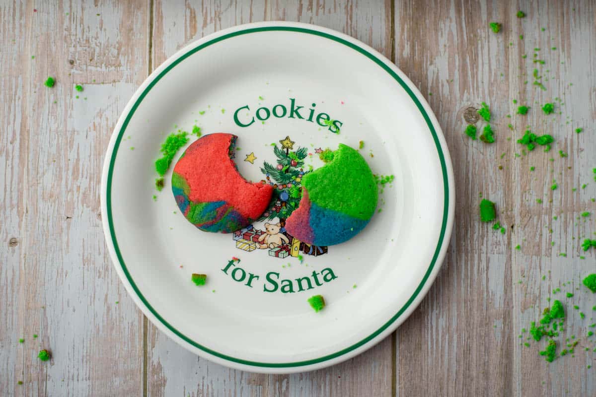 Two colored cookie dough cookies with bites taken out on a plate that says "Cookies for Santa"