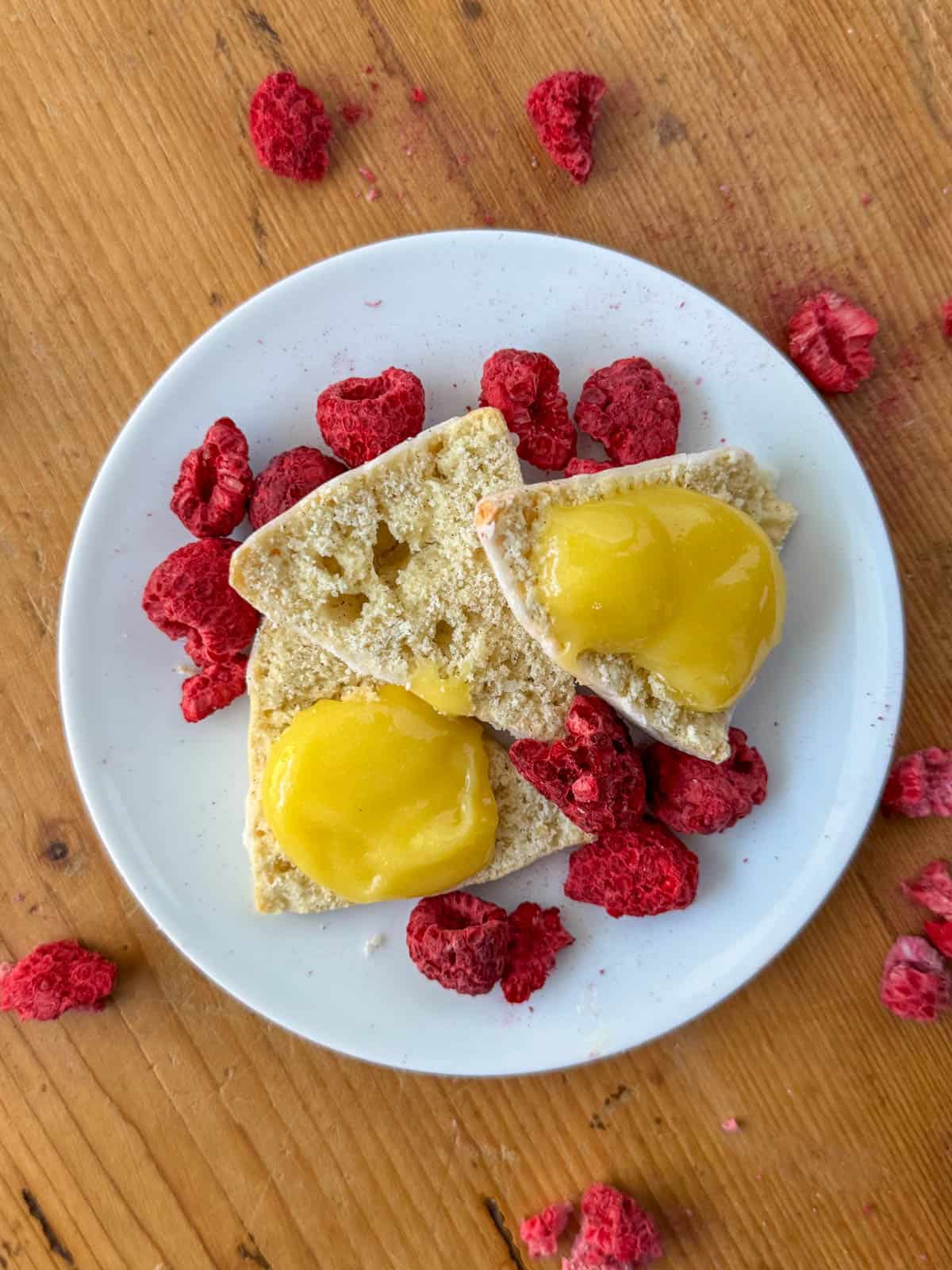 Lemon curd on scones with raspberries sprinkled around on a plate