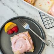 Top view of lemon raspberry sweet roll on plate with pan of sweet rolls in the background