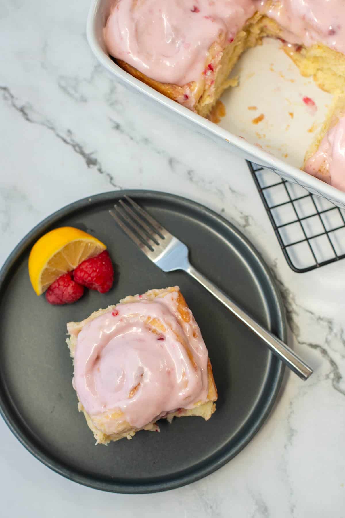 Top view of lemon raspberry sweet roll on plate with pan of sweet rolls in the background