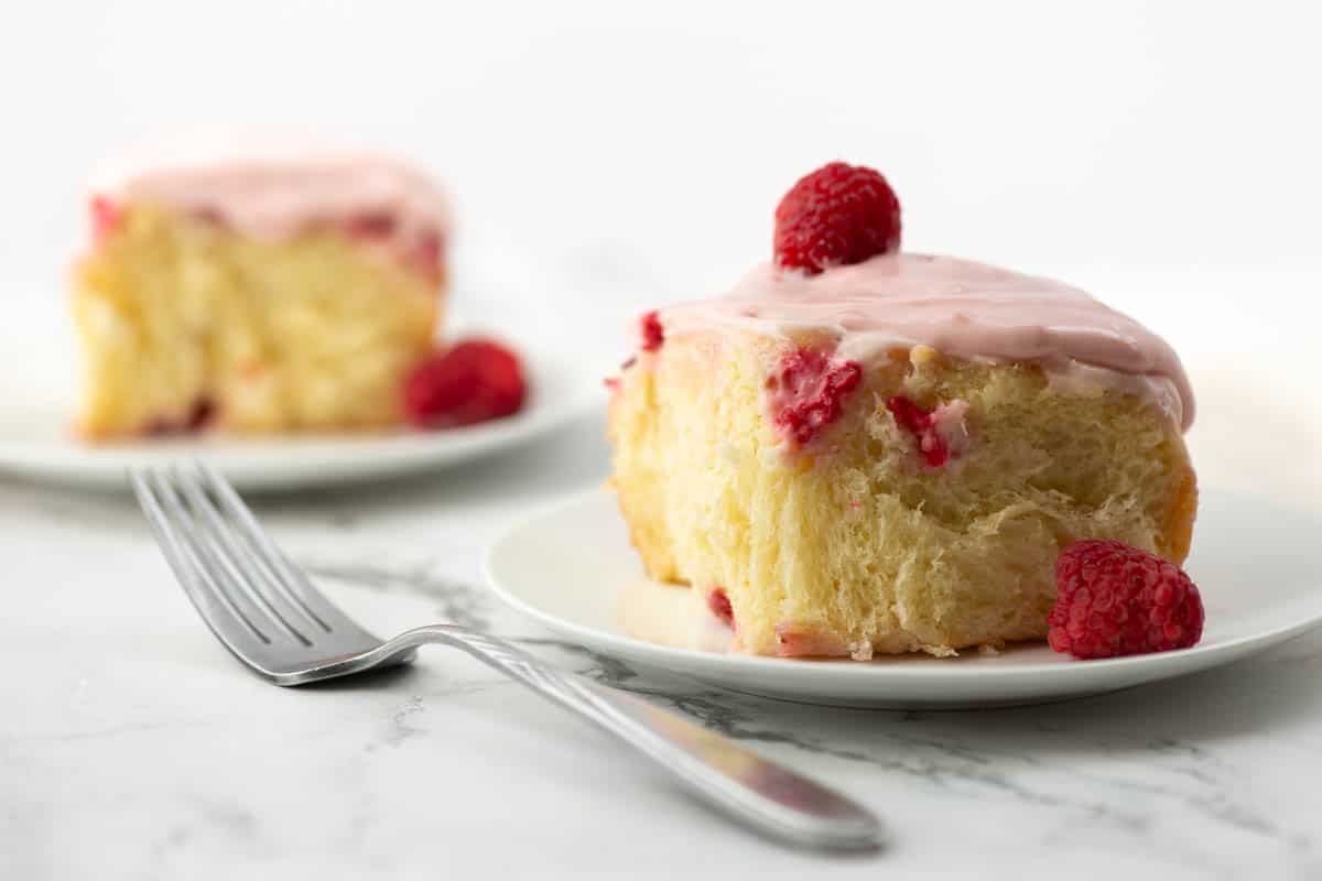 Side view of lemon raspberry sweet roll on a plate with another roll in the background