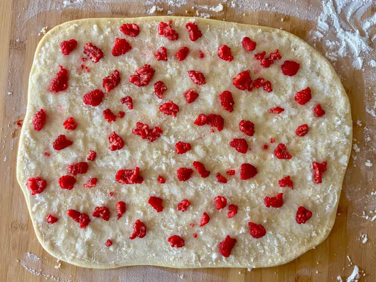 View of sweet dough rolled out with lemon sugar and raspberries sprinkled on top