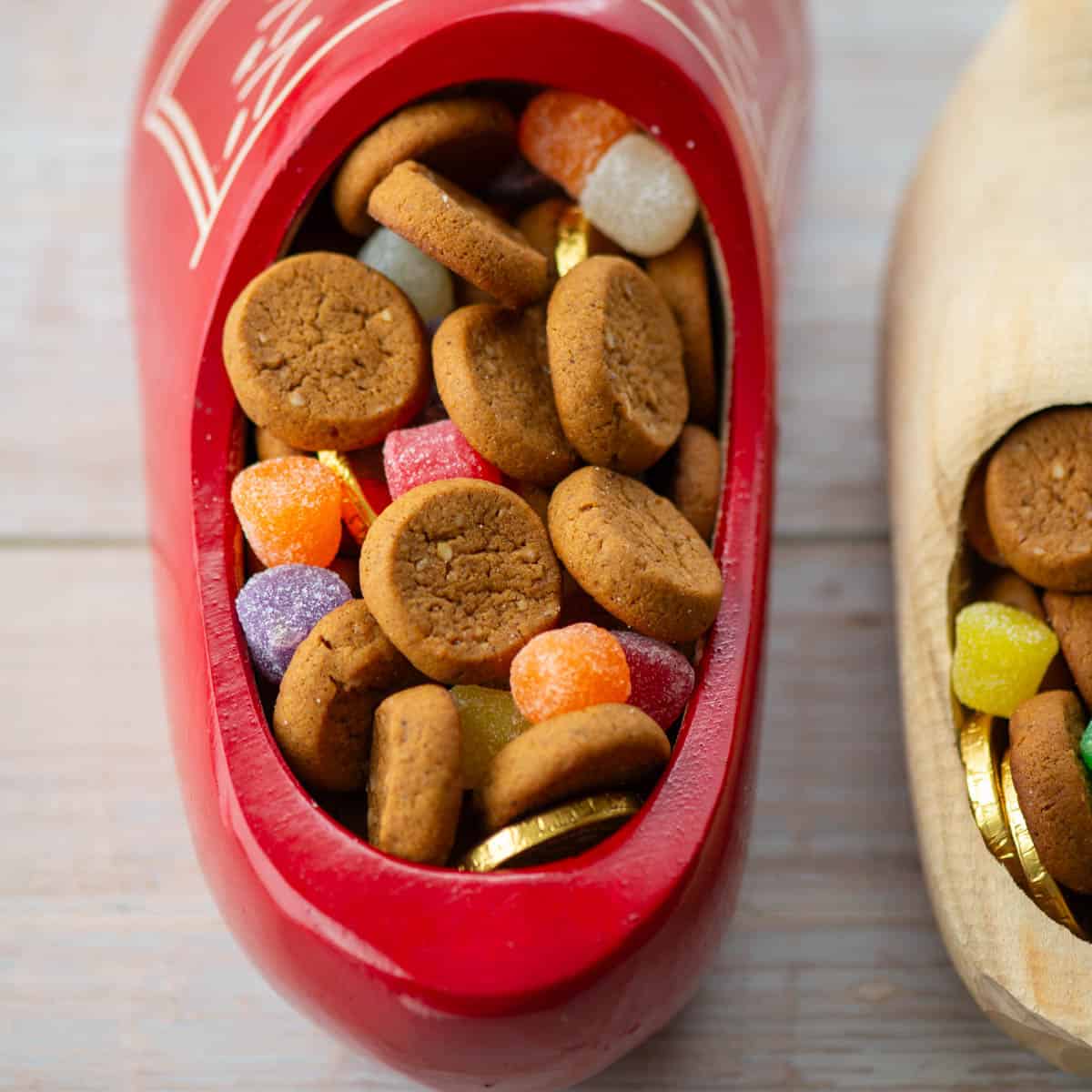 Close up photo of Dutch wooden shoe filled with peppernut cookies, spiced gum drop candies and gold coins with additional shoe to the right