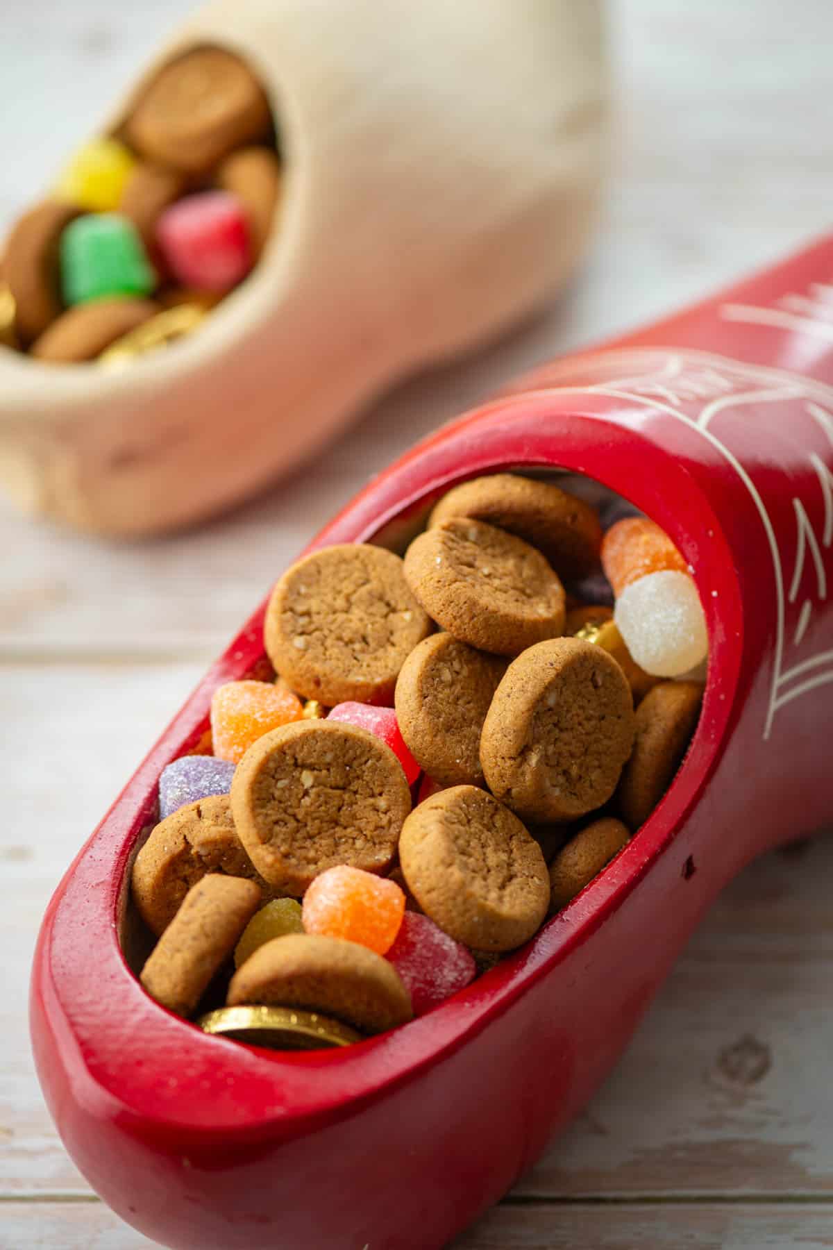 Close up photo of Dutch wooden shoe filled with pepernoten cookies, spiced gum drop candies and gold coins with additional shoe in background