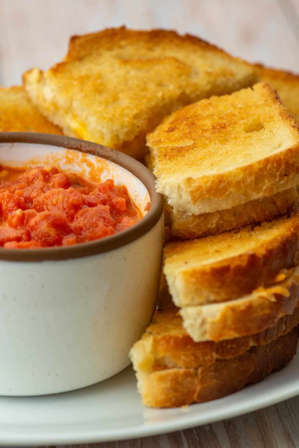 Stacks of cut baked grilled cheese sandwiches next to a bowl of tomato dipping sauce