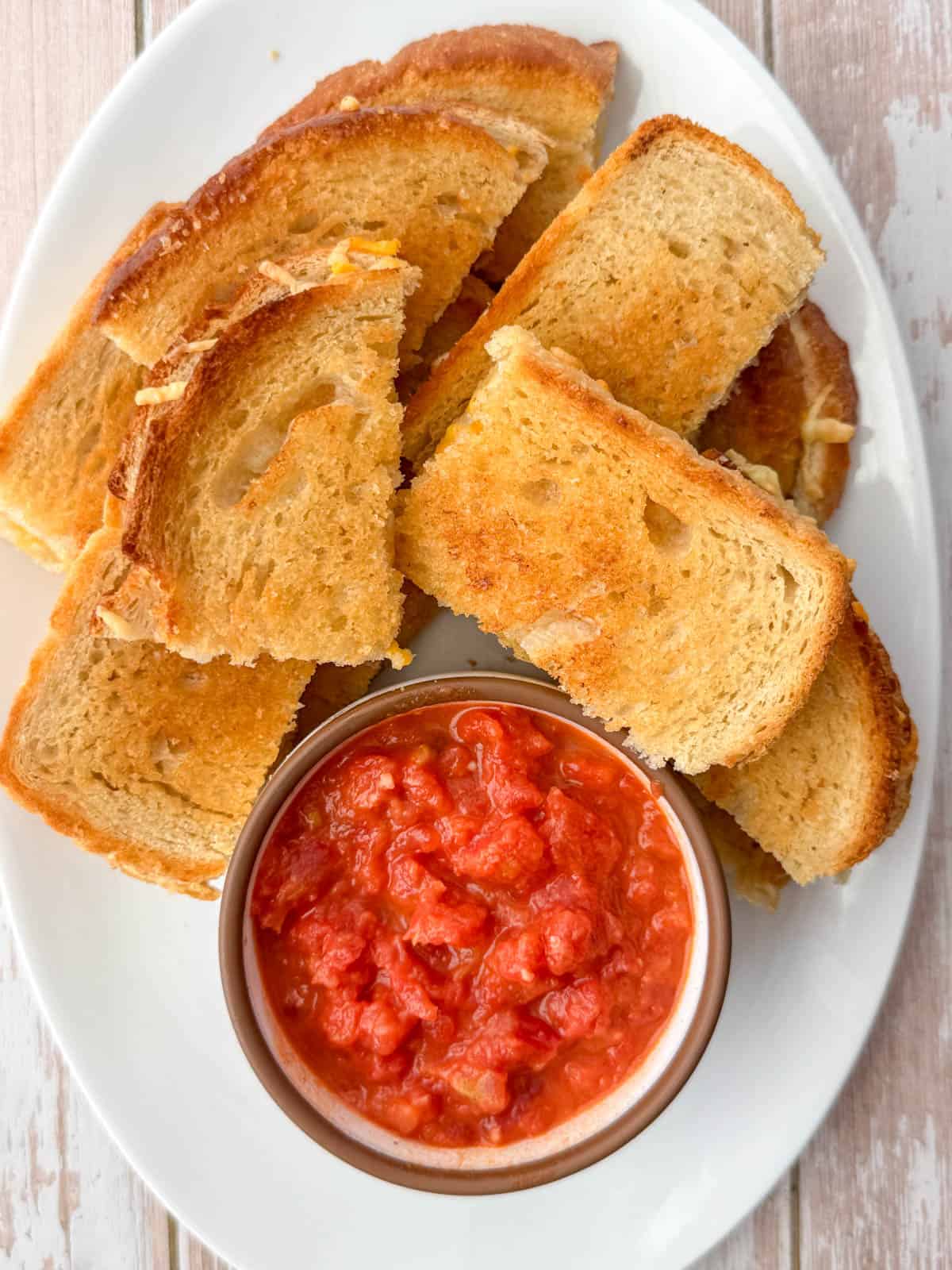 White plate with appetizer size pieces of baked grilled cheese sandwiches with tomato dipping sauce