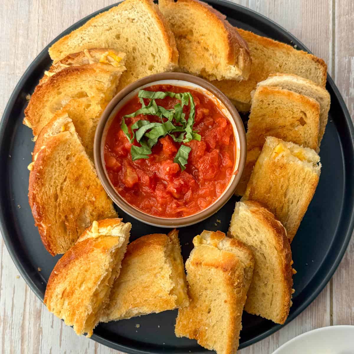 Grey plate with appetizer size pieces of baked grilled cheese sandwiches with tomato dipping sauce