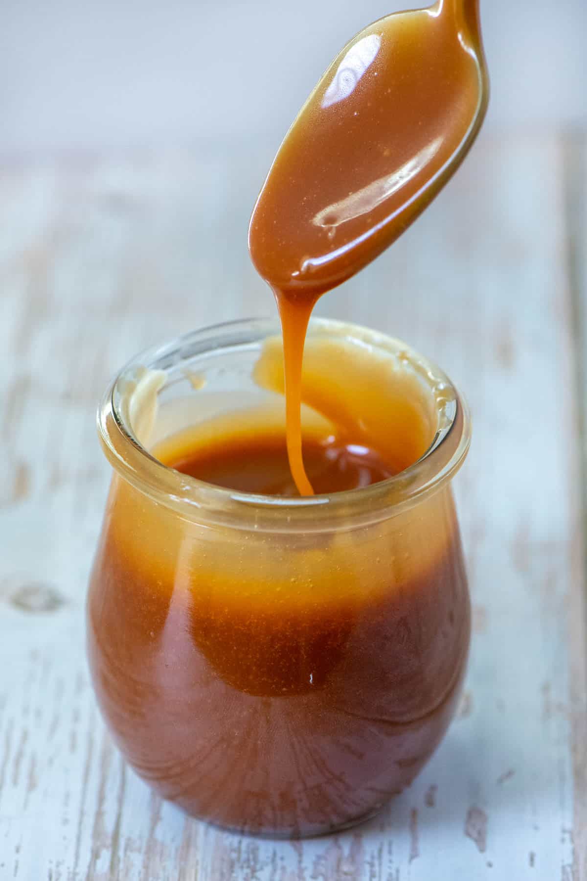 Spoon of homemade salted caramel sauce dripping into jar of homemade salted caramel sauce