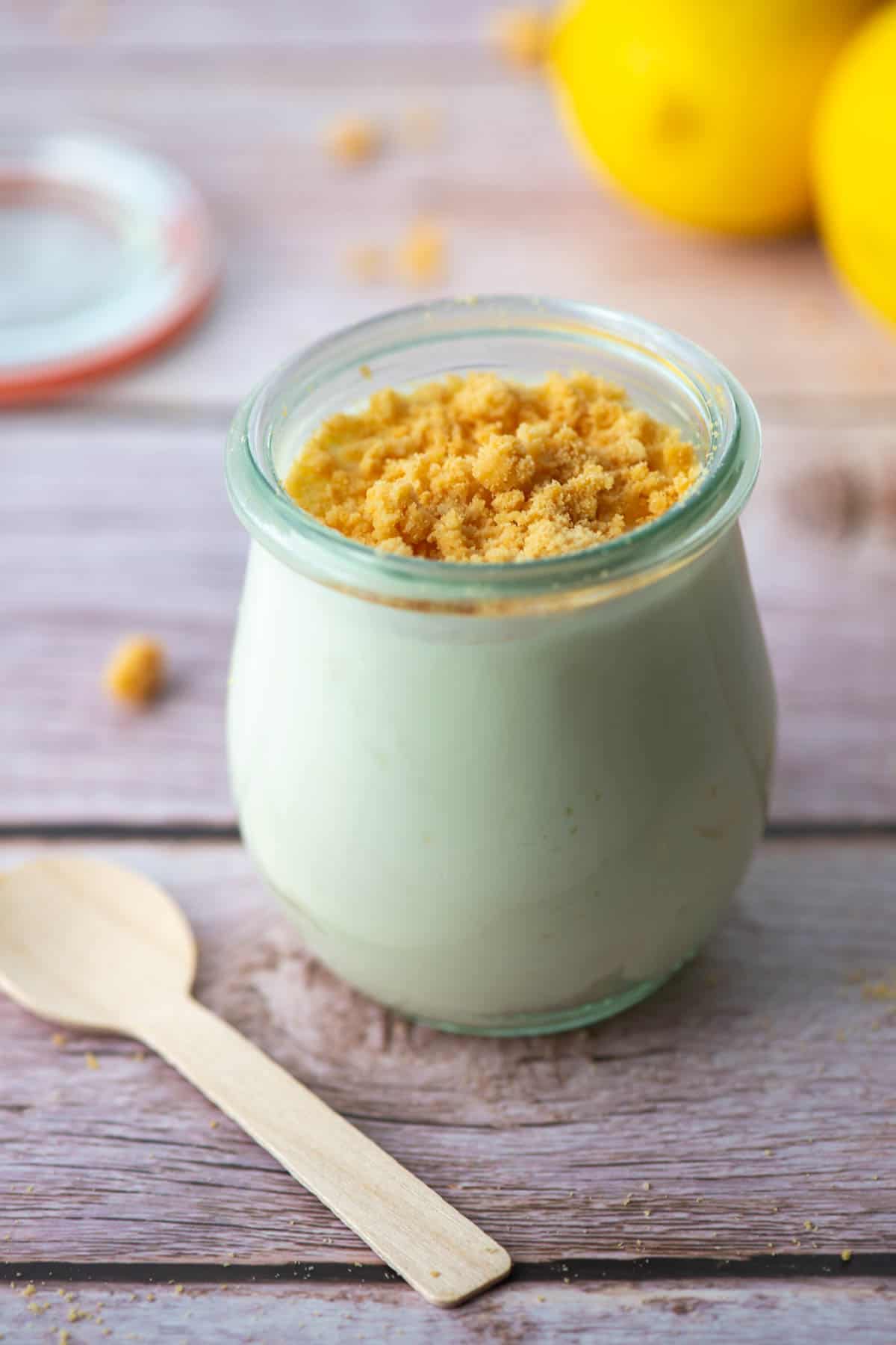 Jar of keto mini lemon cheesecake next to a wooden spoon with lemons in the background