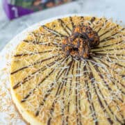 Overhead view of full Samoas cheesecake topped with chocolate, toasted coconut and Samoas cookies with box of Samoas cookies blurred in the background