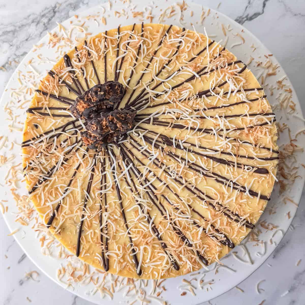 Overhead view of full Samoas cheesecake topped with chocolate, toasted coconut and Samoas cookies