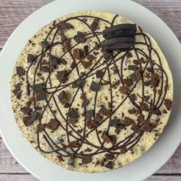 Close up photo of Thin Mints cheesecake topped with chocolate drizzle, crumbled Thin Mints and two full Thin Mints