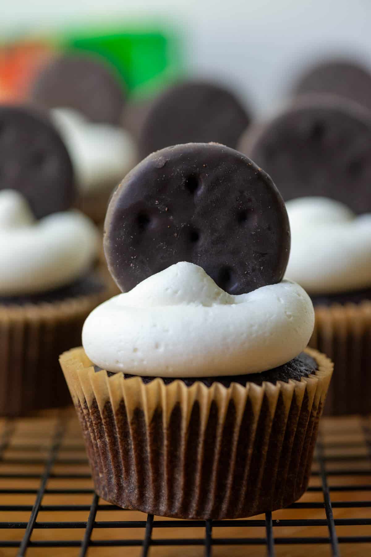 Photo of many Thin Mints Cupcakes on a cooling rack with a box of Thin Mints cookies in the background