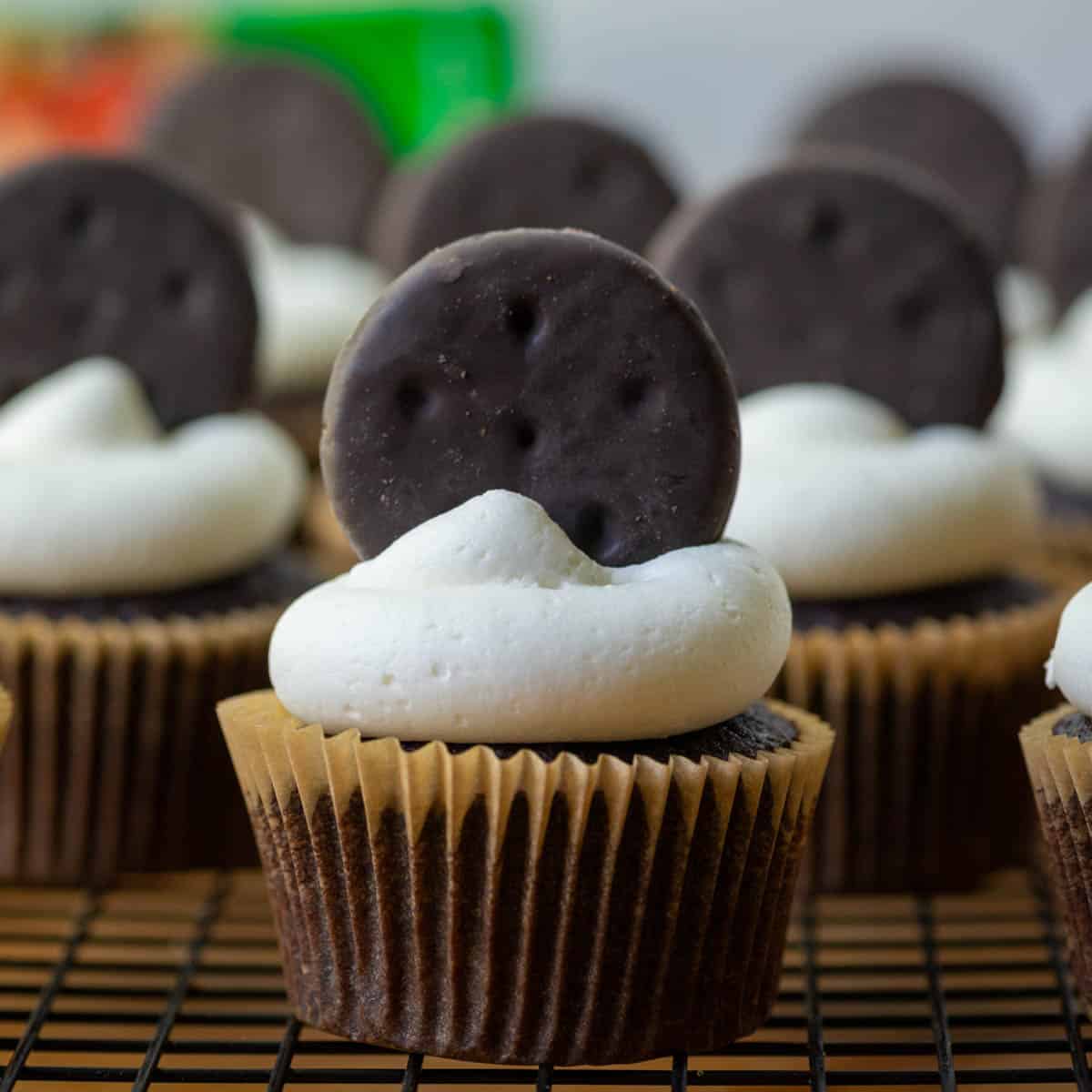 Photo of many Thin Mints Cupcakes on a cooling rack with a box of Thin Mints cookies in the background