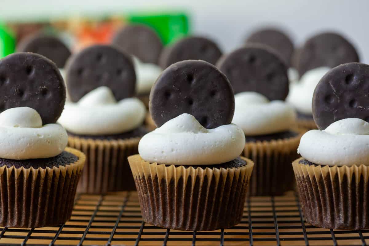 Photo of many Thin Mints Cupcakes on a cooling rack with a box of Thin Mints cookies in the background