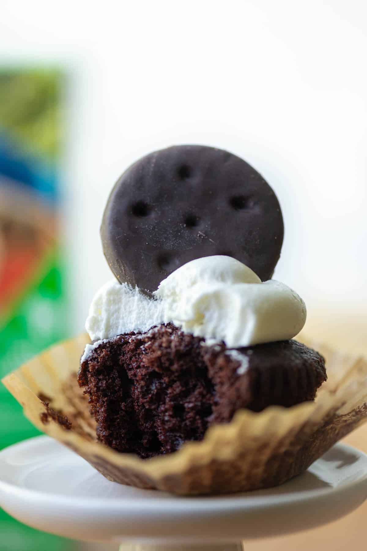 Close up photo of one Thin Mints cupcake with bite taken out with a box of Thin Mints cookies in the background