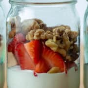 Side view of mason jar filled with greek yogurt, strawberries and walnuts