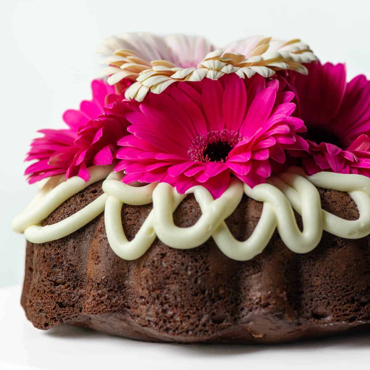 Side view of chocolate bundt cake decorated with cream cheese frosting drips and flowers