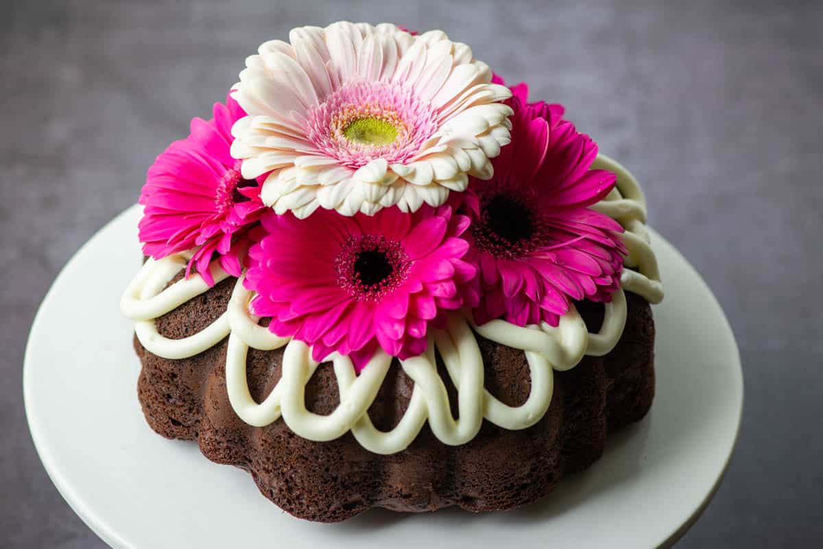 Overhead view of entire chocolate chocolate chip bundt cake with frosting drips and a floral cake topper