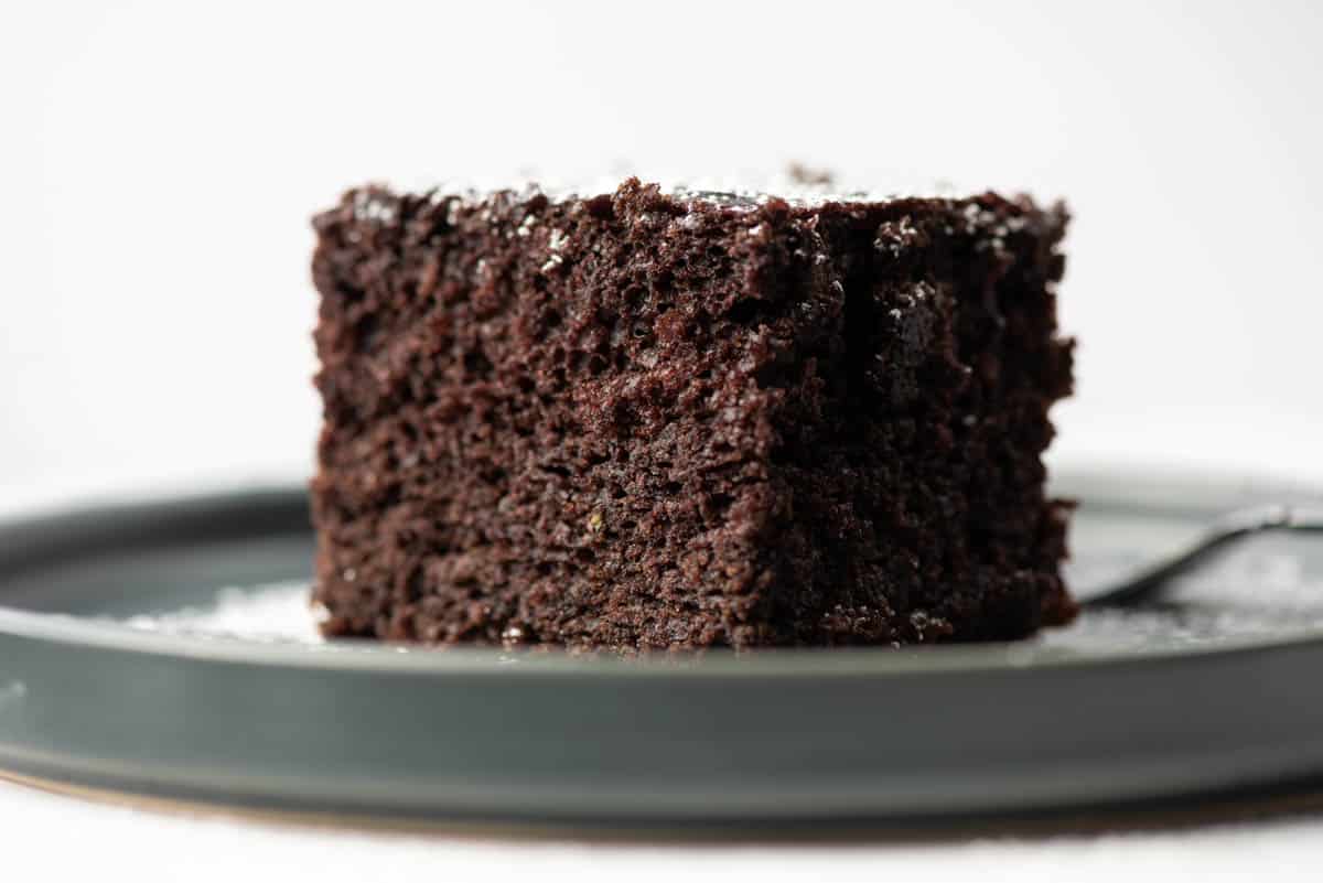 Side view of slice of chocolate zucchini cake topped with powdered sugar on a plate