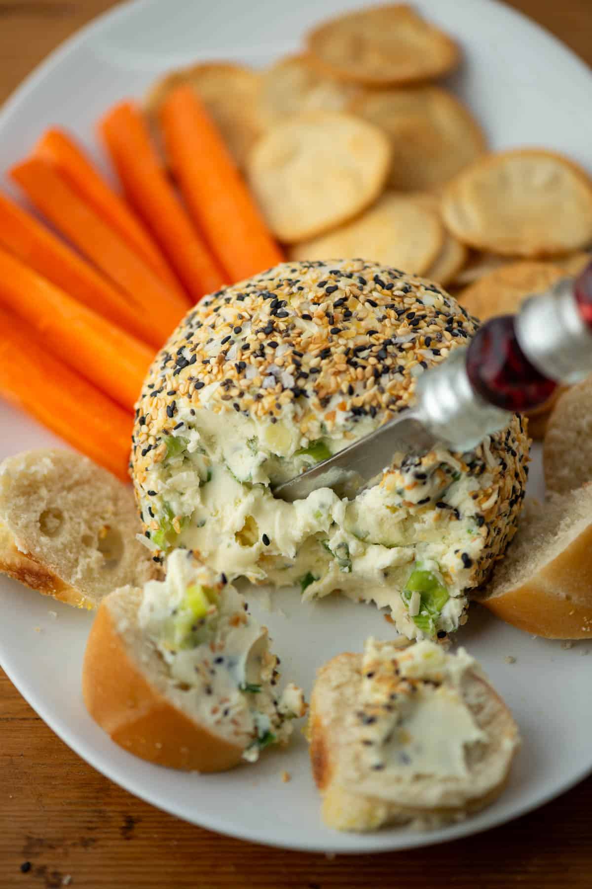 Photo of an Everything Bagel Cheeseball on a plate next to bagel slices, carrots and pita crackers