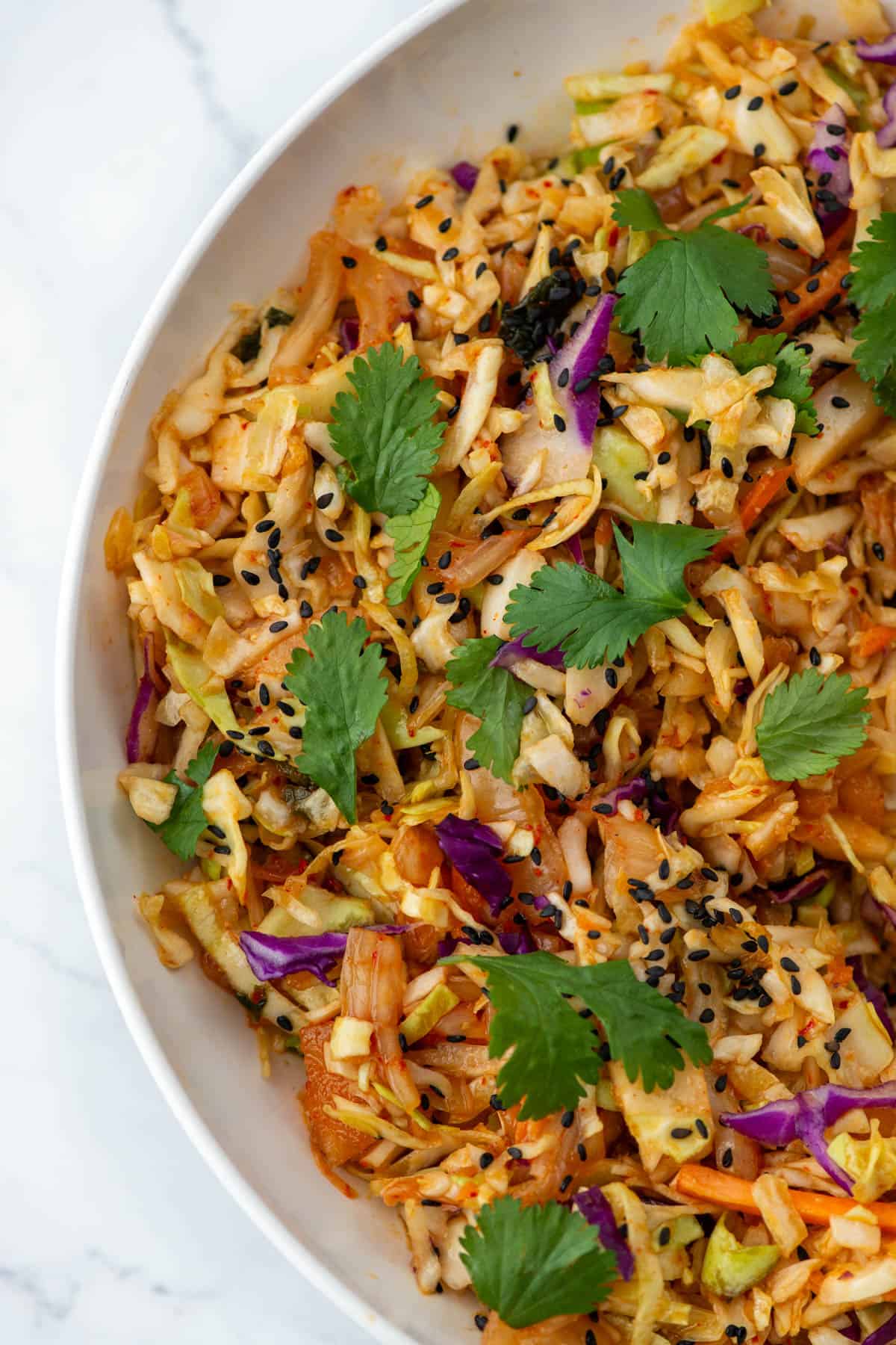 Partial bowl of kimchi slaw garnished with black sesame seeds and cilantro