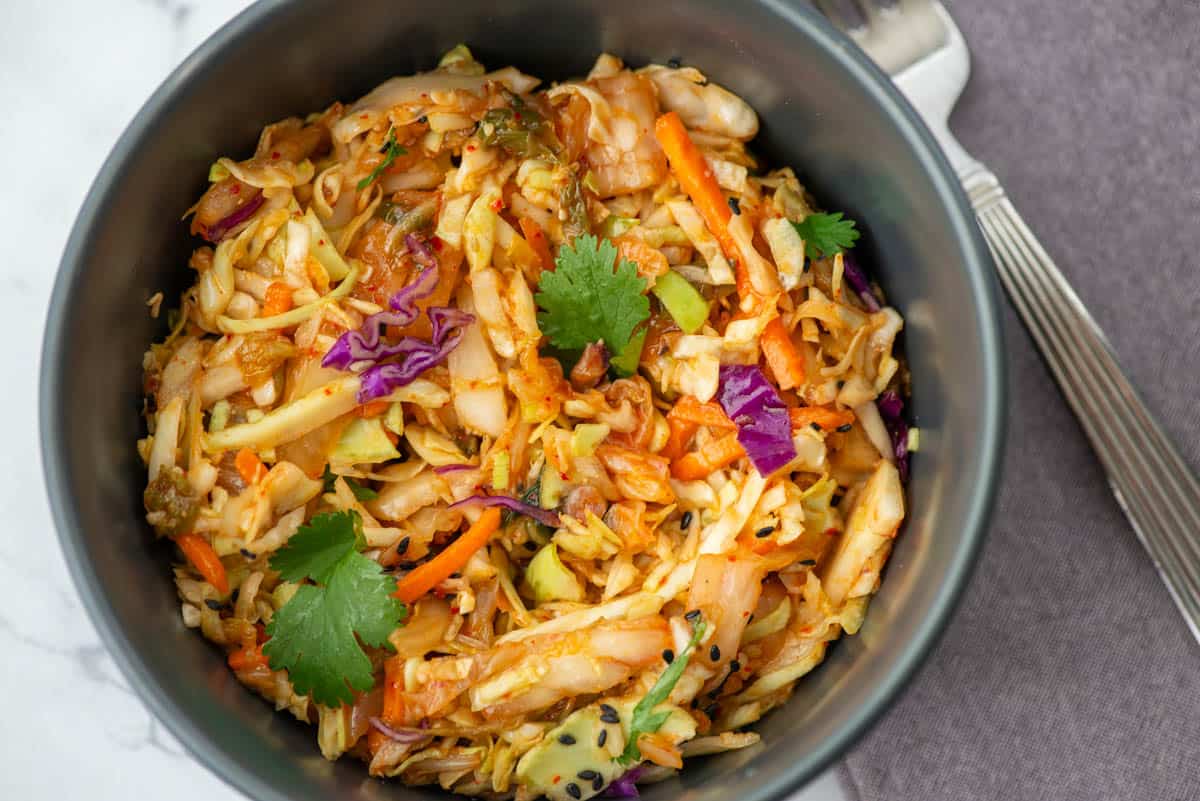 Overhead photo close up photo of kimchi slaw garnished with cilantro leaves and black sesame seeds