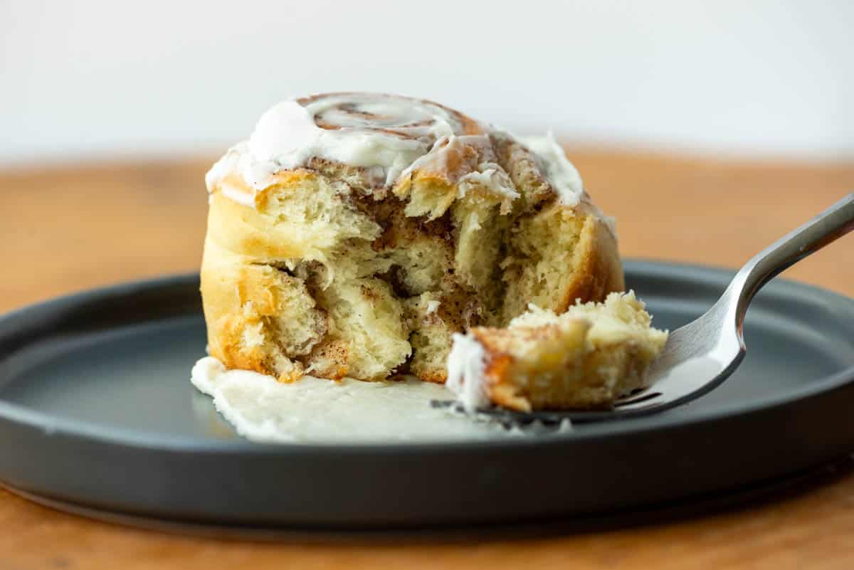 Side view of cinnamon roll on plate with a bite on a fork.