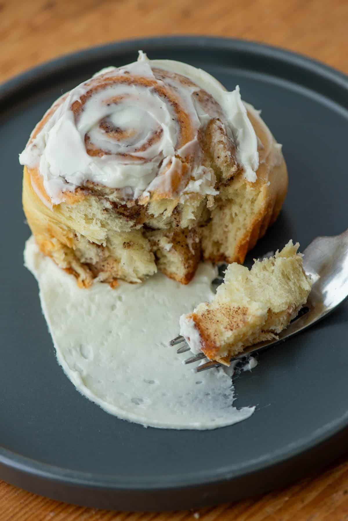 Top view of cinnamon roll on plate with a bite on a fork.