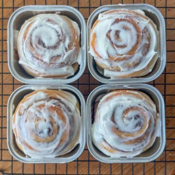 Overhead view of four cinnamon rolls in mini square baking cups on top of a cooling rack.