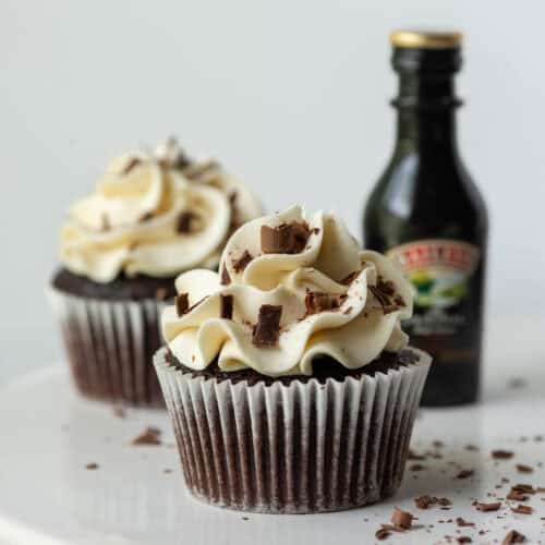 One chocolate Baileys Irish Cream cupcake with Baileys buttercream frosting in front of another cupcake and a mini bottle of Baileys Irish Cream