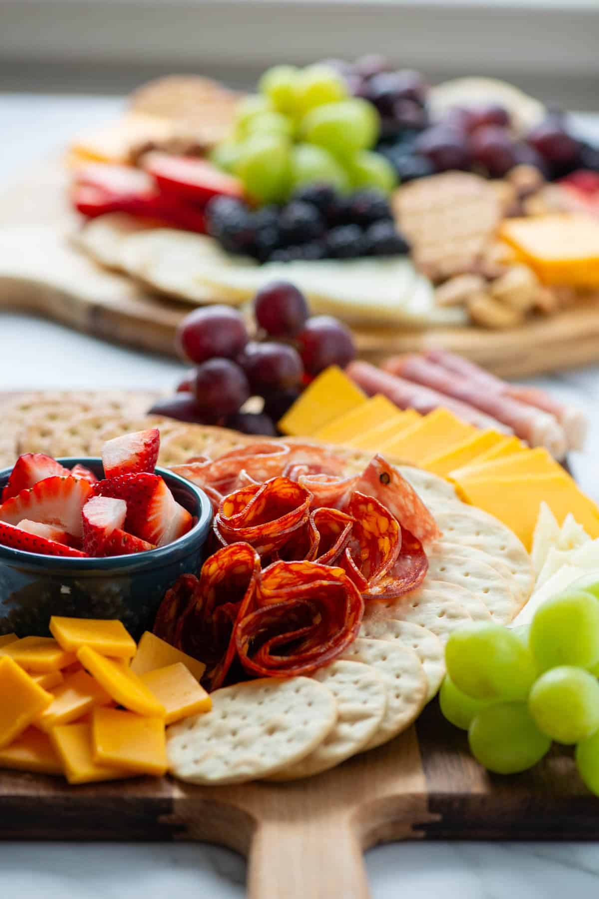 Side view of a charcuterie board with cheeses, meats, fruits and crackers with another full charcuterie board in the background 