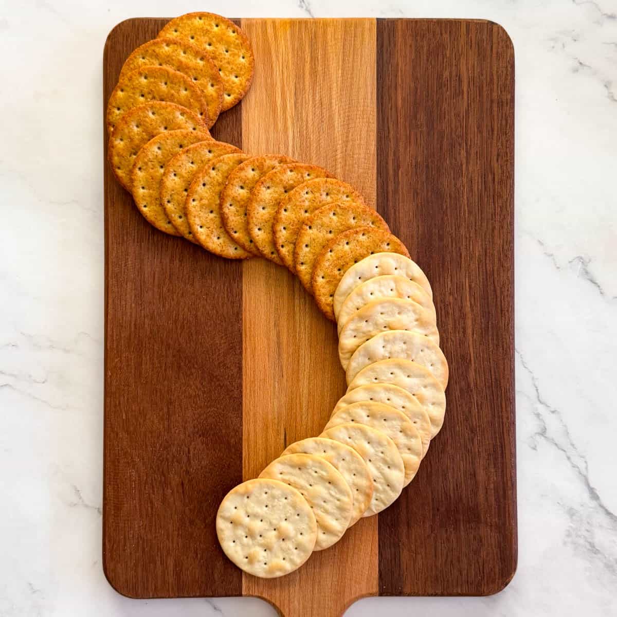 Step 1 of making a charcuterie board: place crackers in an S shape