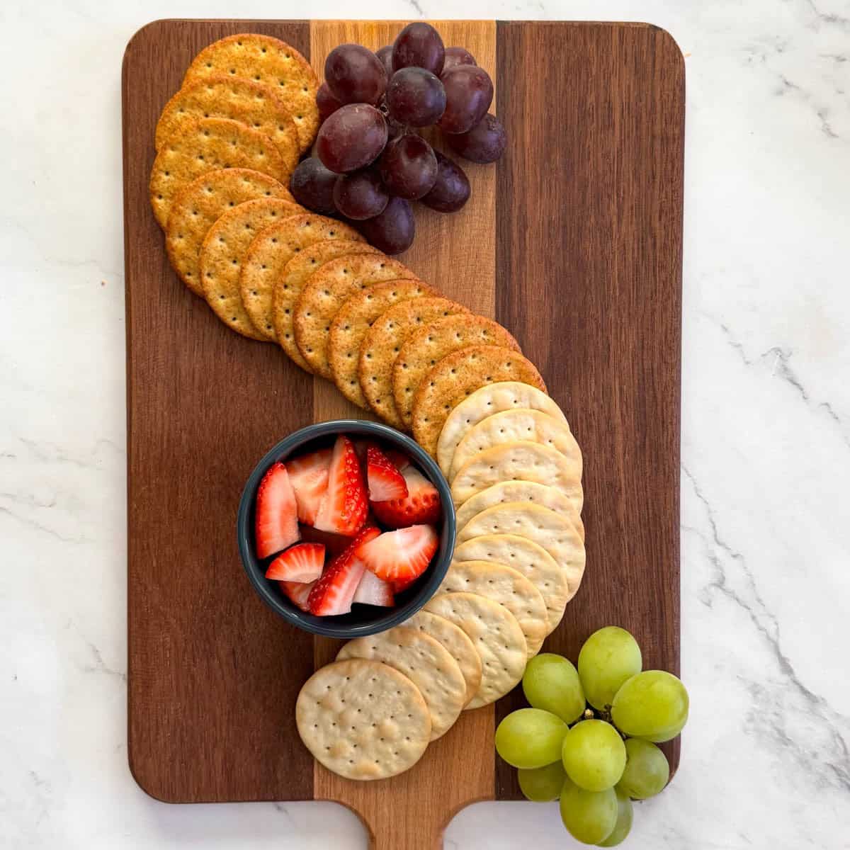 Step 2 of making a charcuterie board: add fruits near crackers on board