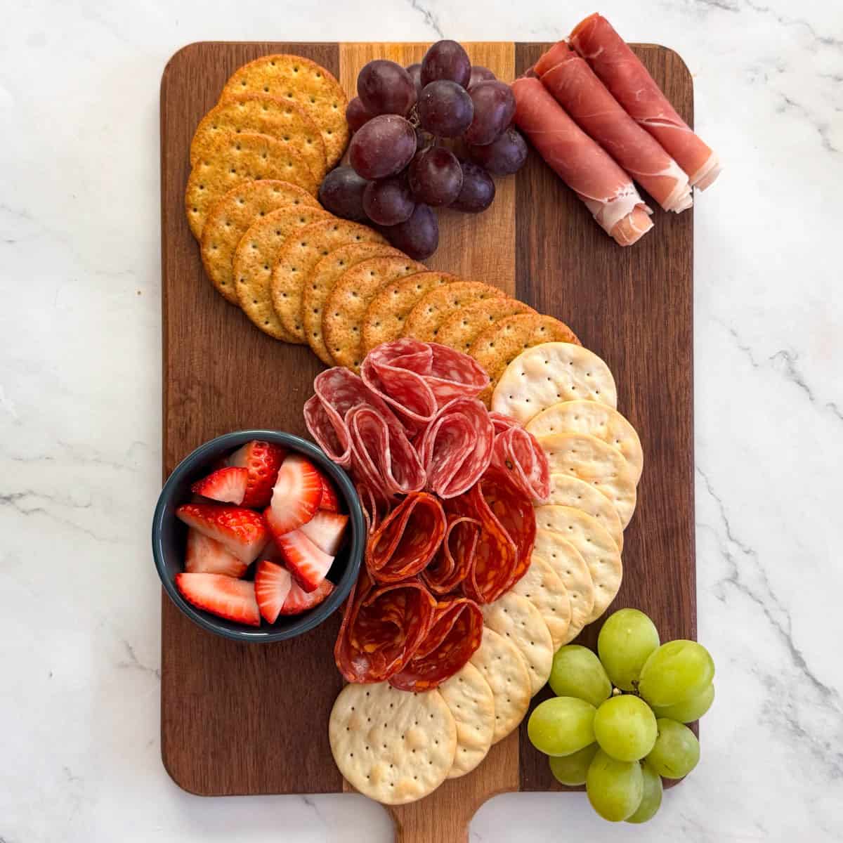 Step 3 of making a charcuterie board: add meats to crackers and fruits on the board