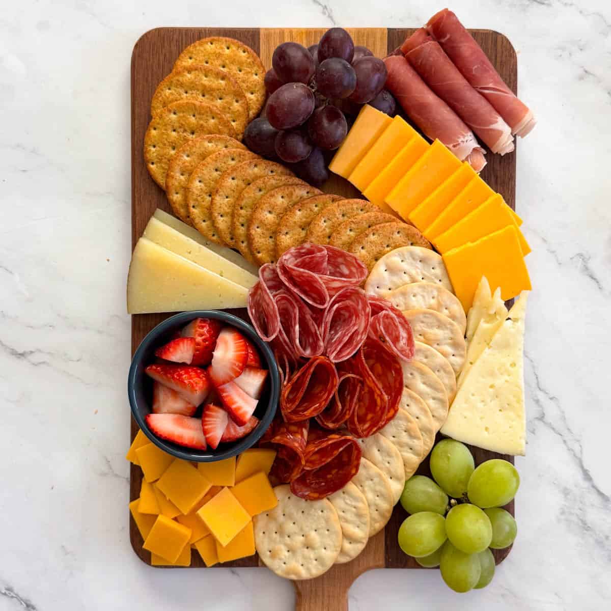 Step 4 of making a charcuterie board: fill in any remaining open spaces on the board with the cheeses