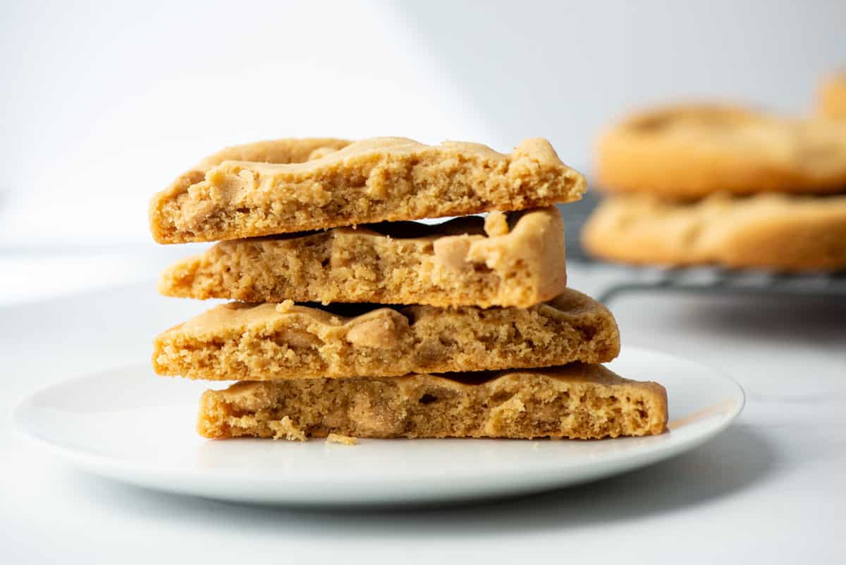 Side view of 4 giant peanut butter cookies on a plate with more blurred cookies in the background