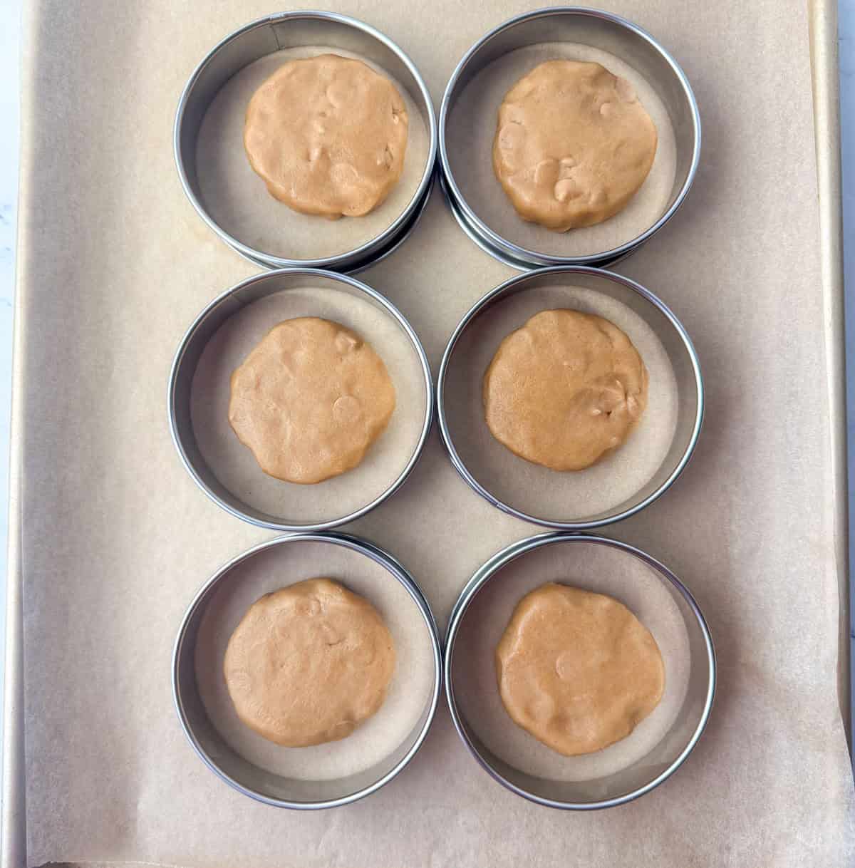Overhead view of six flattened peanut butter cookie dough balls inside of six bakery rings