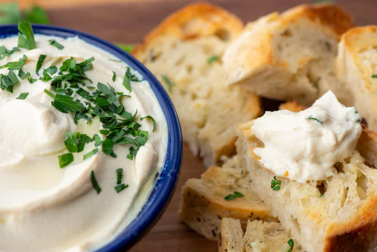 Bowl of whipped tofu garnished with finely shopped parsley next to pieces of garlic bread 