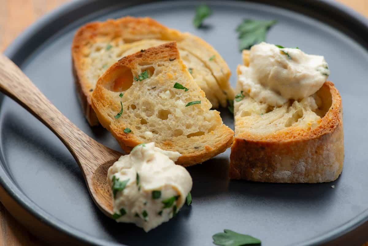 Pieces of garlic bread and a spoon topped with whipped tofu and chopped parsley on a grey plate